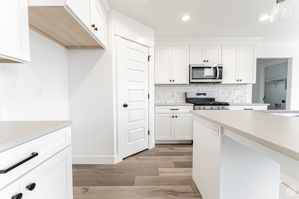 Kitchen with appliances with stainless steel finishes, light wood-style floors, decorative backsplash, light countertops, and white cabinetry