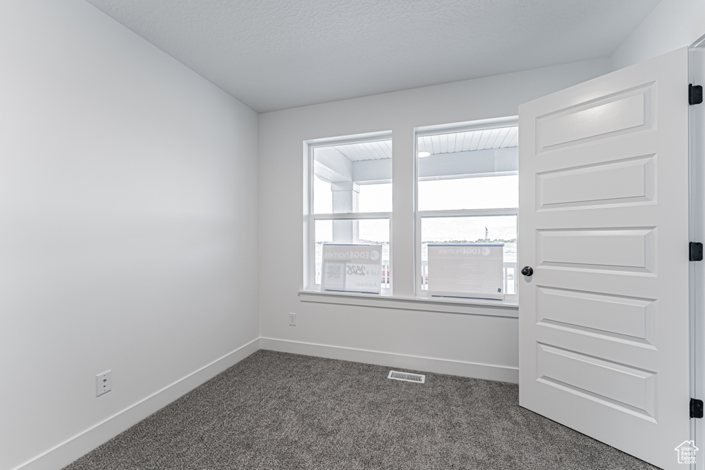 Spare room featuring dark colored carpet and baseboards