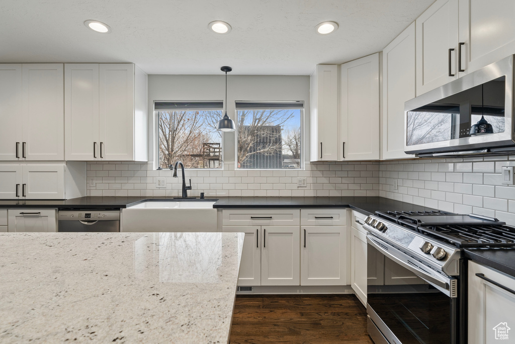 Kitchen featuring dark wood-style floors, backsplash, appliances with stainless steel finishes, white cabinets, and a sink