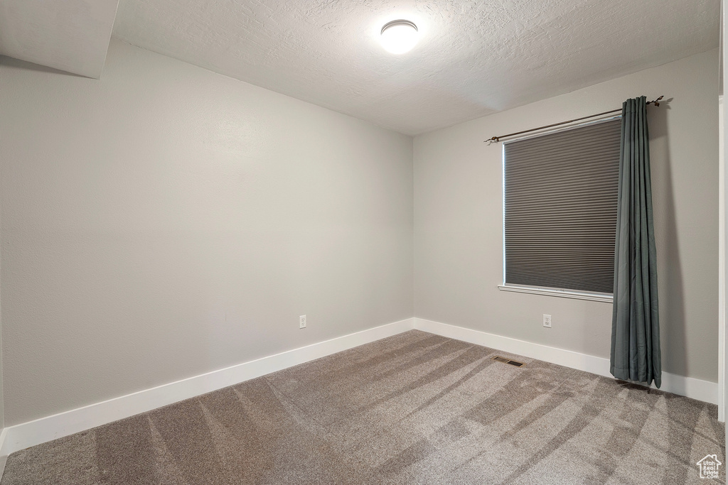 Empty room featuring a textured ceiling, carpet, visible vents, and baseboards