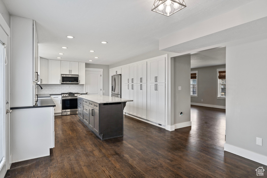 Kitchen with white cabinetry, appliances with stainless steel finishes, decorative backsplash, and dark wood-style flooring