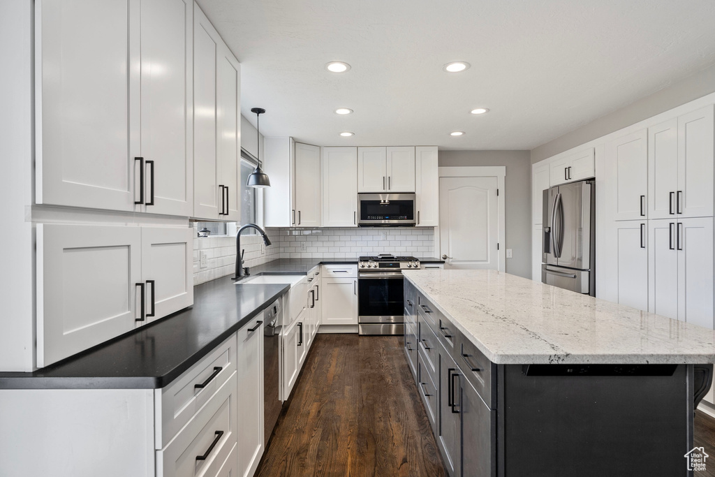 Kitchen with tasteful backsplash, appliances with stainless steel finishes, a center island, white cabinetry, and a sink