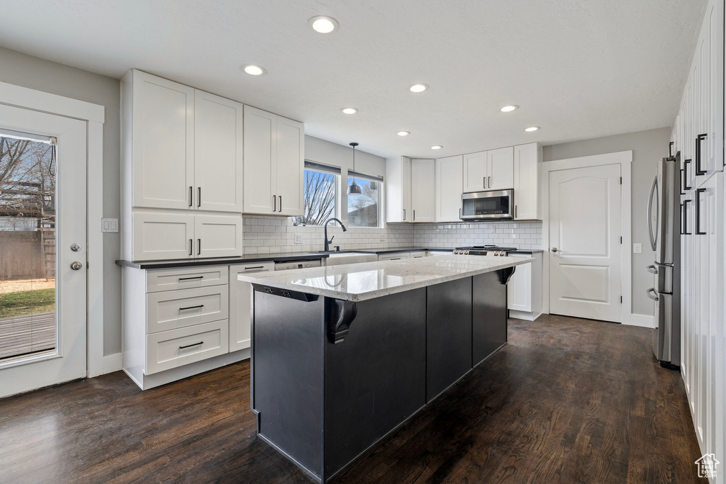 Kitchen with dark wood-style floors, stainless steel appliances, light stone counters, and a center island