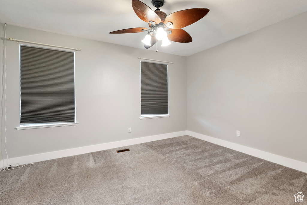 Carpeted empty room with baseboards, visible vents, and a ceiling fan