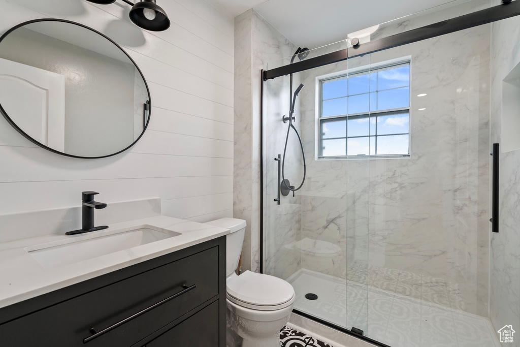 Full bath with wooden walls, a stall shower, vanity, and toilet