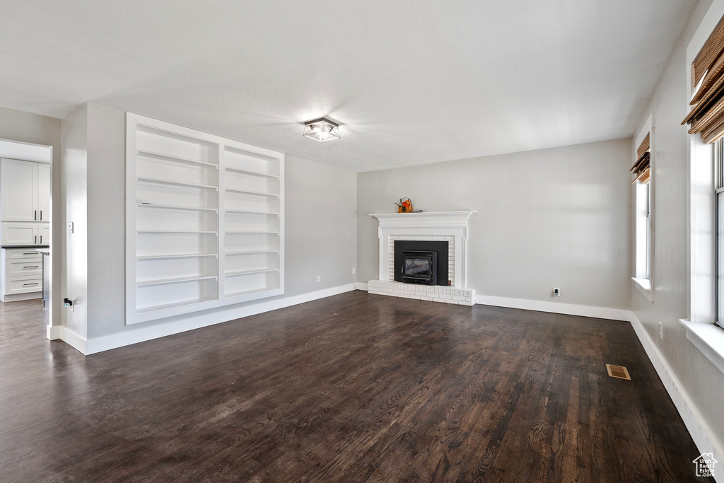 Unfurnished living room featuring dark wood-style floors, a brick fireplace, and baseboards