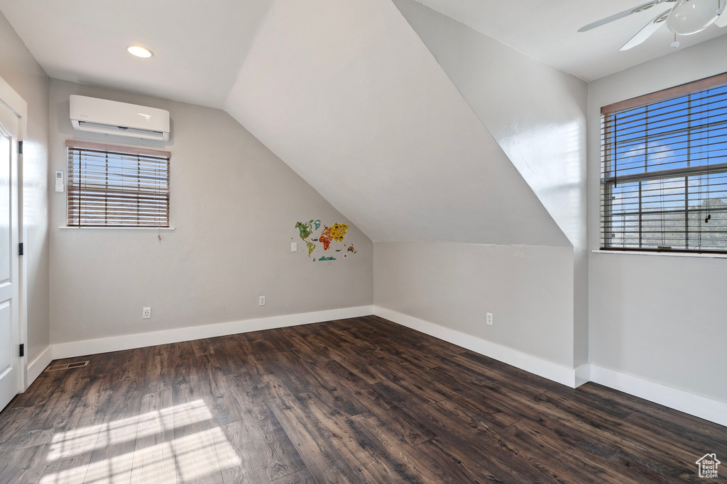 Bonus room with dark wood-type flooring, an AC wall unit, plenty of natural light, and baseboards