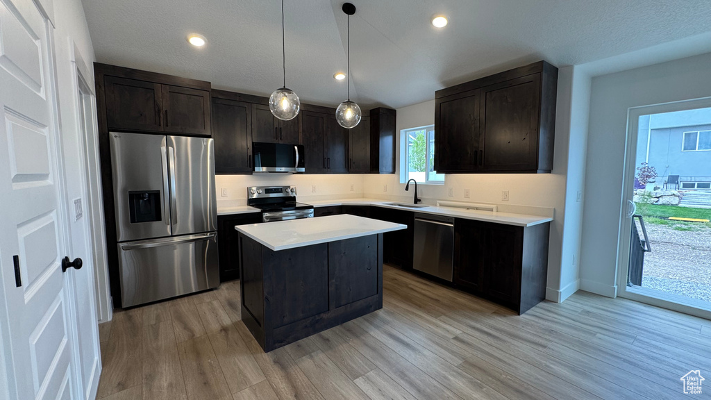 Kitchen with a kitchen island, light wood-style floors, light countertops, a sink, and appliances with stainless steel finishes