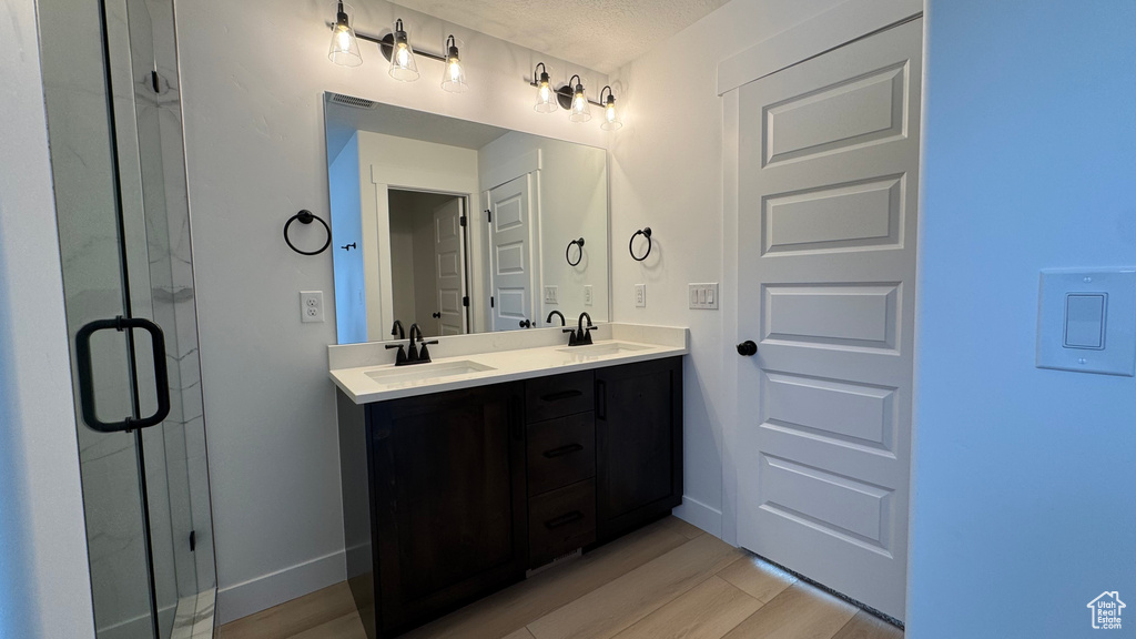 Bathroom with double vanity, a shower stall, a sink, and wood finished floors