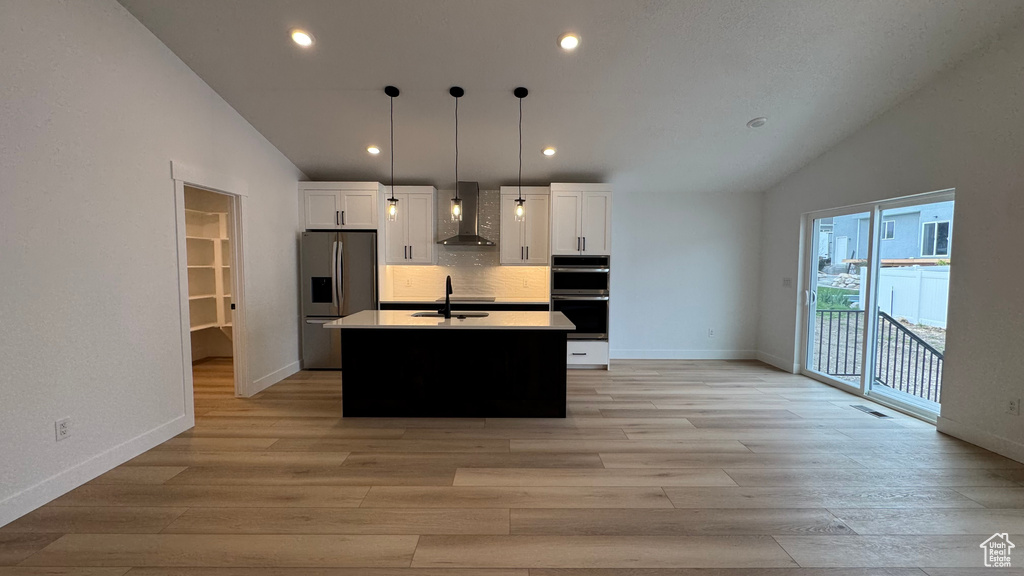 Kitchen featuring appliances with stainless steel finishes, white cabinetry, wall chimney exhaust hood, and lofted ceiling
