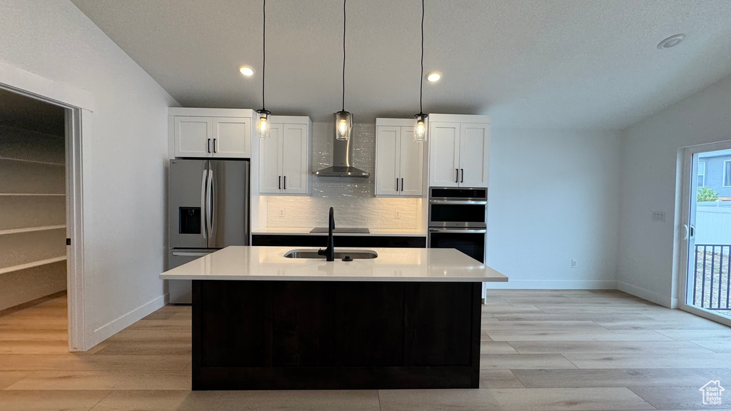Kitchen featuring white cabinets, stainless steel appliances, baseboards, and wall chimney exhaust hood