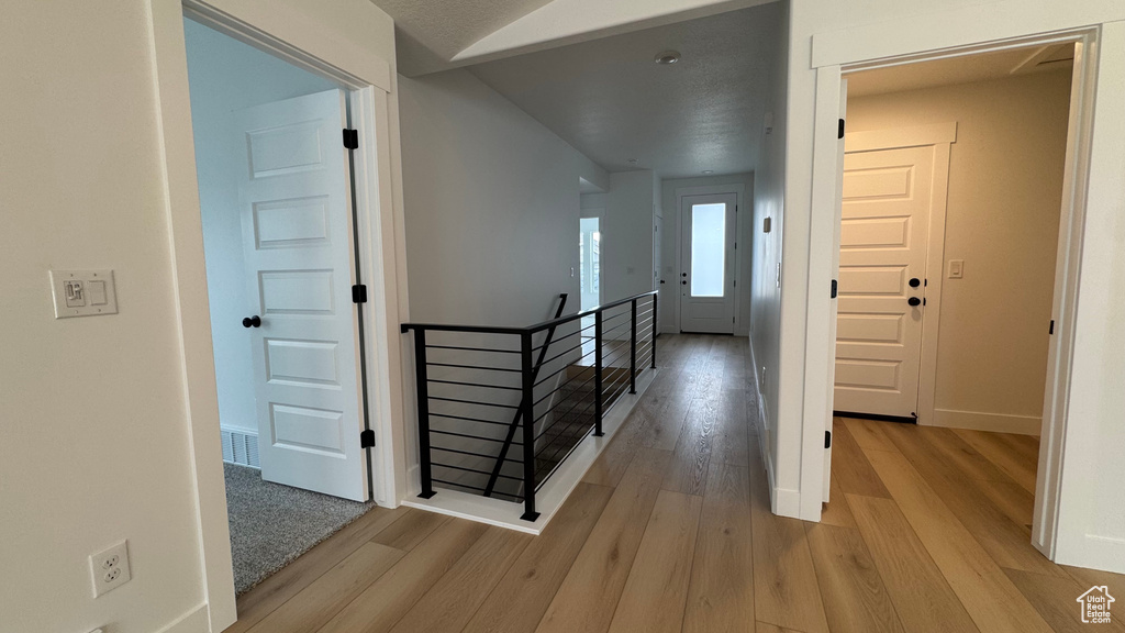 Hall featuring baseboards, light wood-style flooring, visible vents, and an upstairs landing
