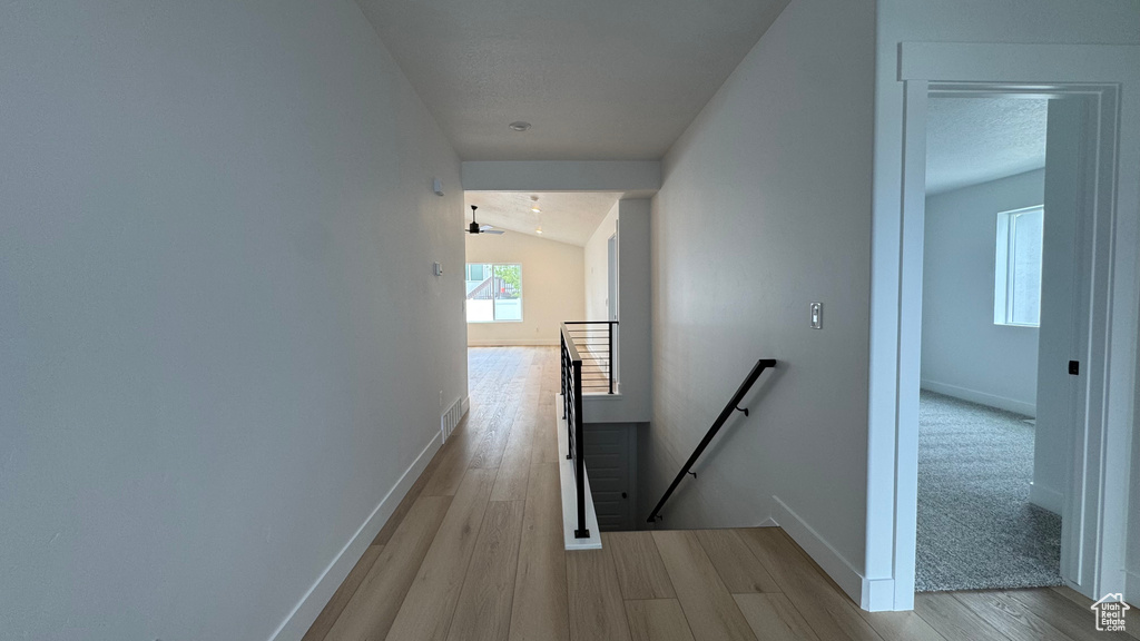 Hallway featuring baseboards, lofted ceiling, wood finished floors, and an upstairs landing