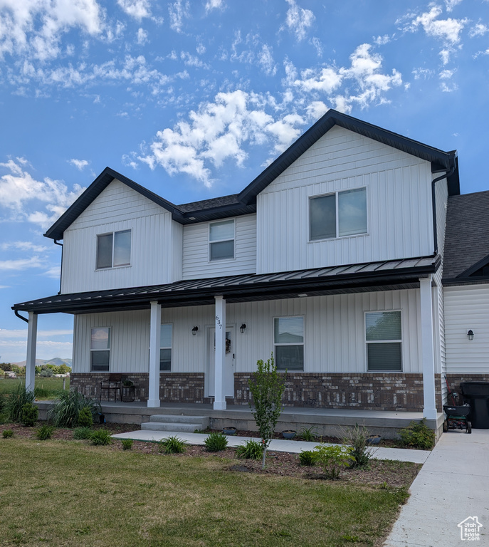 View of front of house with a porch, a standing seam roof, brick siding, metal roof, and a front lawn