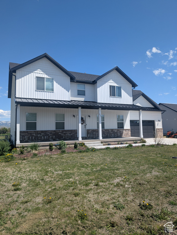 Modern farmhouse style home featuring a standing seam roof, an attached garage, covered porch, metal roof, and a front yard