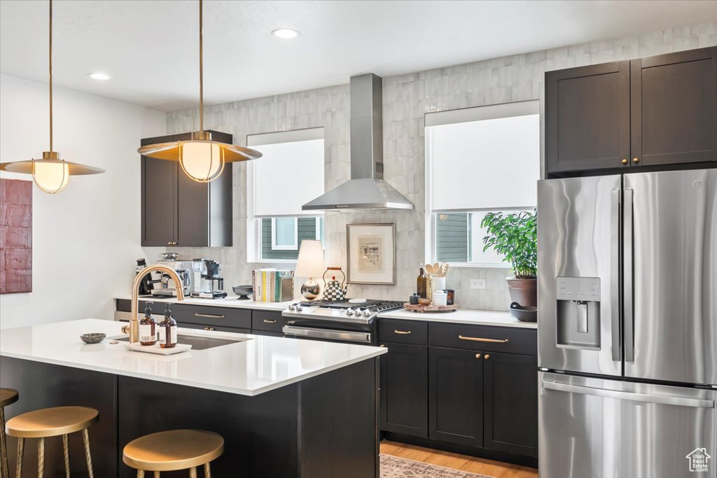 Kitchen featuring a breakfast bar, stove, a sink, stainless steel refrigerator with ice dispenser, and wall chimney exhaust hood