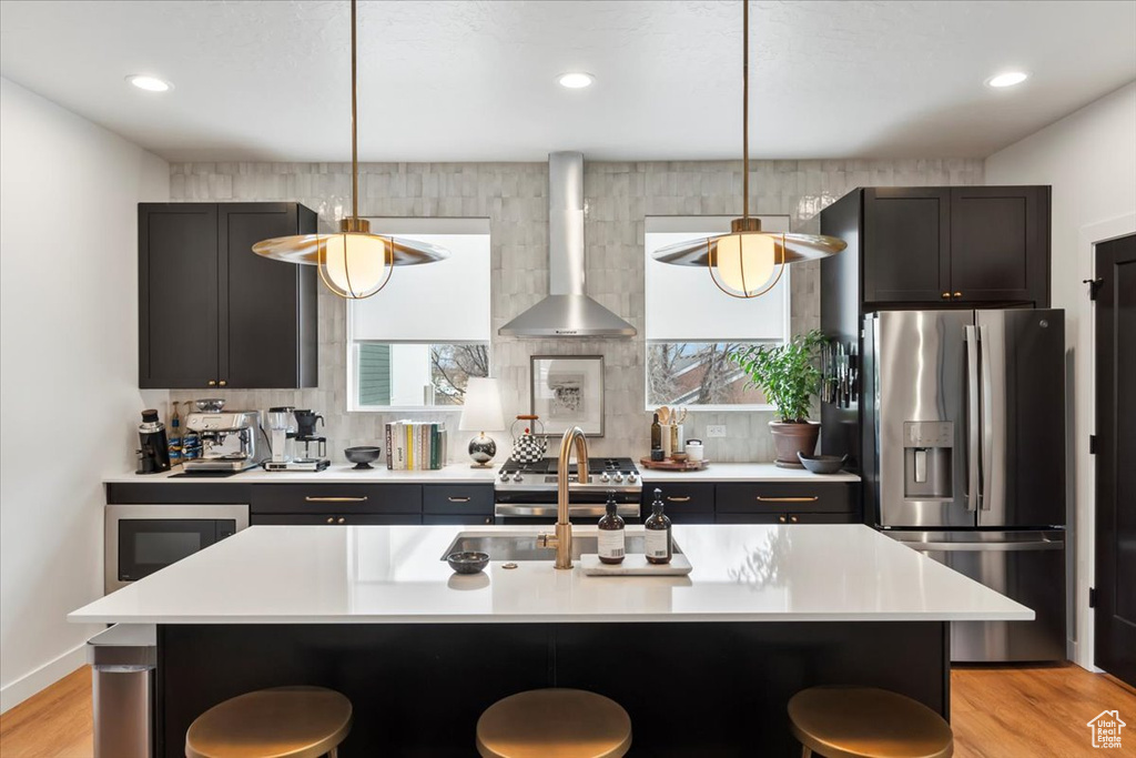 Kitchen featuring wall chimney exhaust hood, appliances with stainless steel finishes, light countertops, and a kitchen breakfast bar