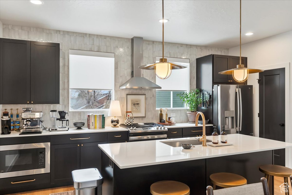 Kitchen featuring wall chimney exhaust hood, a breakfast bar area, stainless steel appliances, light countertops, and a sink