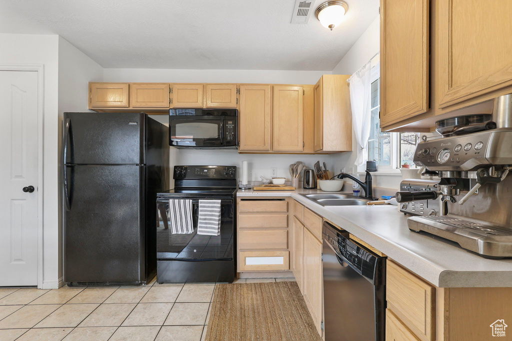 Kitchen featuring light countertops, visible vents, light brown cabinets, a sink, and black appliances