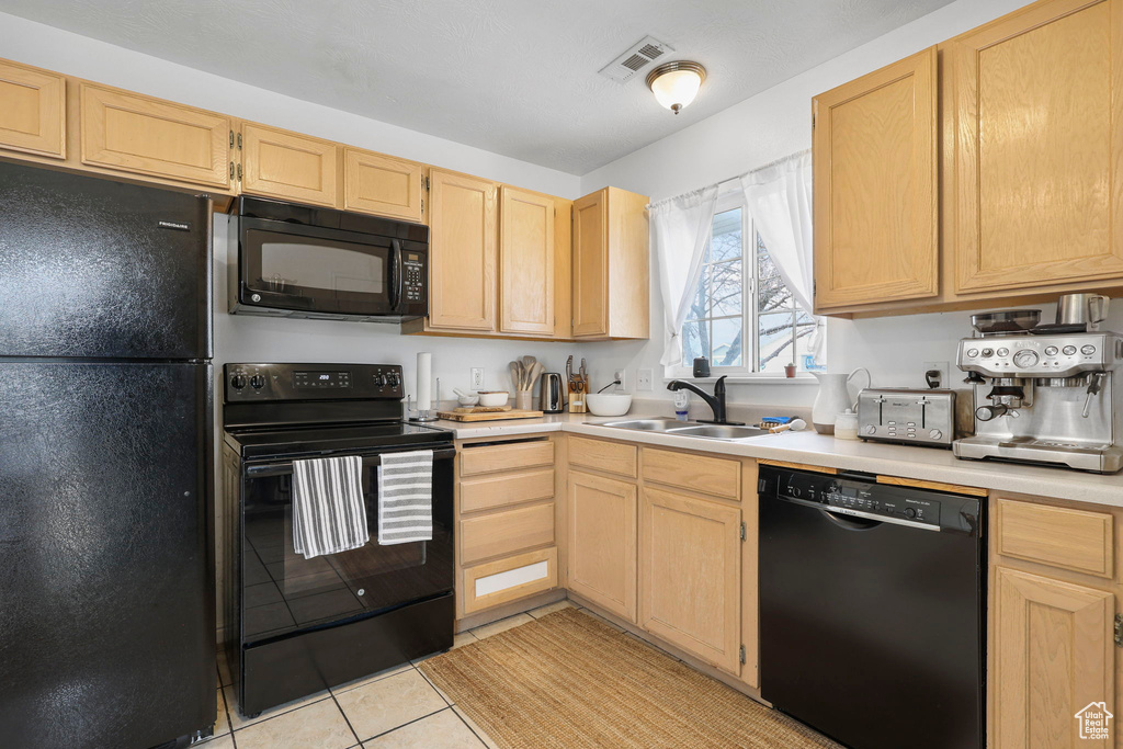 Kitchen with black appliances, light brown cabinets, light countertops, and a sink