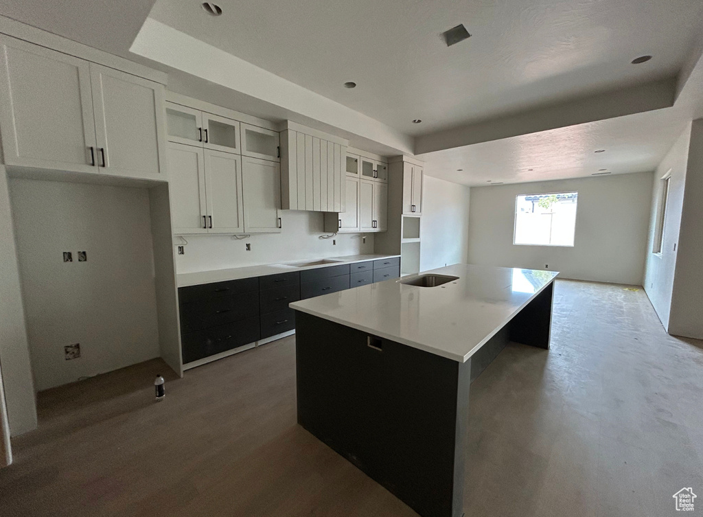 Kitchen with glass insert cabinets, stovetop, a sink, a kitchen island with sink, and white cabinetry
