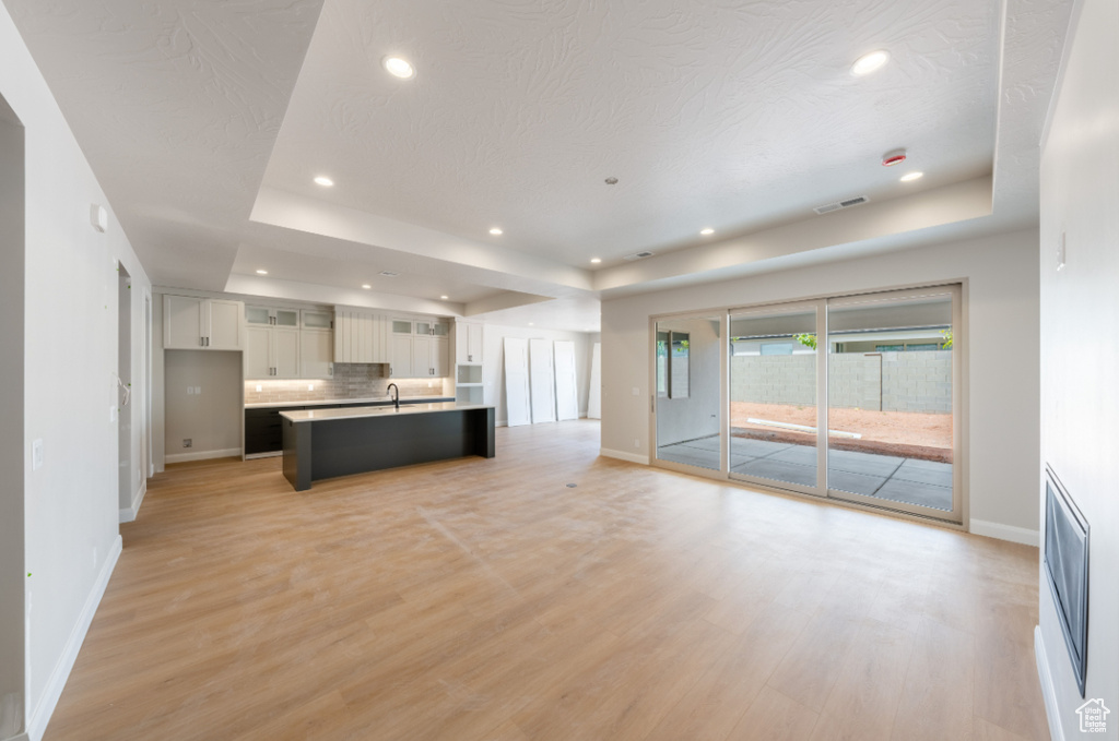 Unfurnished living room featuring a tray ceiling, baseboards, light wood finished floors, and recessed lighting