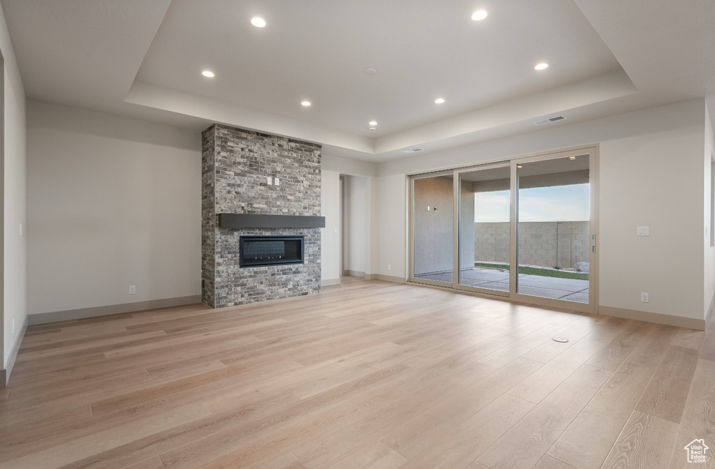 Unfurnished living room with a fireplace, baseboards, a raised ceiling, light wood-style floors, and recessed lighting