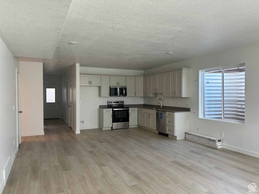 Kitchen featuring appliances with stainless steel finishes, a textured ceiling, light wood-style floors, and baseboards