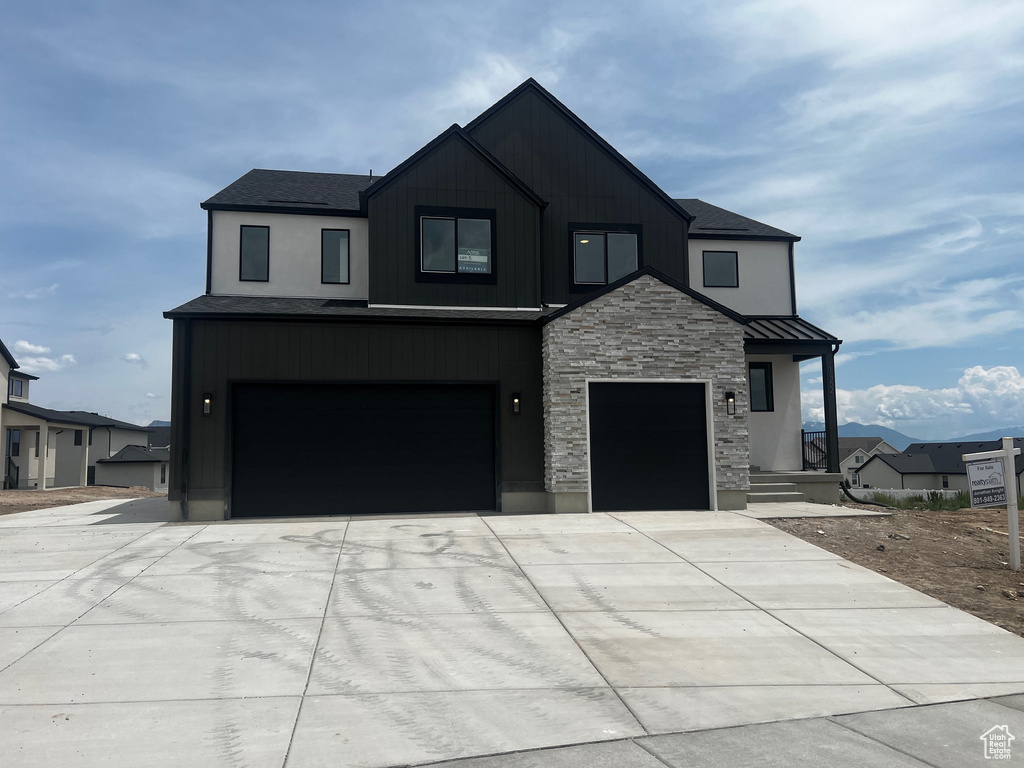 Modern farmhouse with stone siding, driveway, an attached garage, and a standing seam roof
