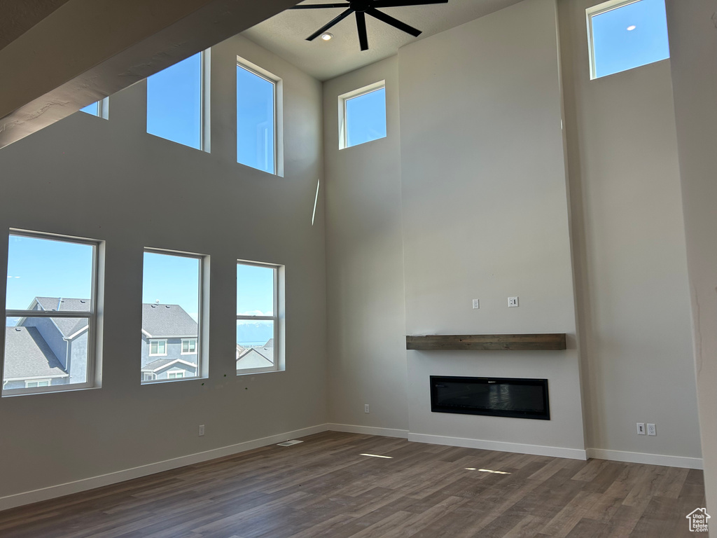 Unfurnished living room featuring wood finished floors, a towering ceiling, baseboards, a glass covered fireplace, and ceiling fan