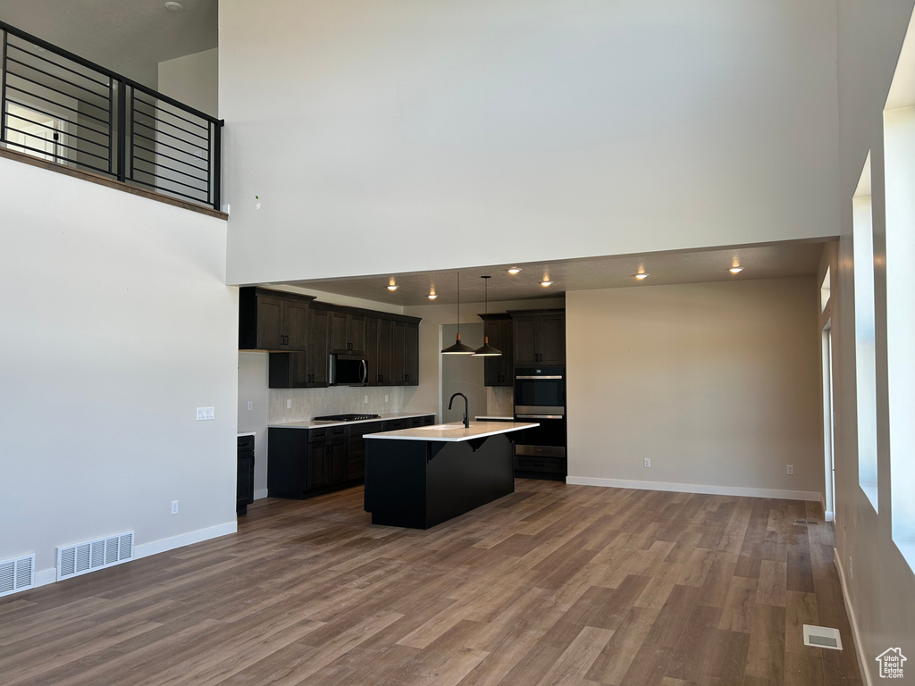 Kitchen with stainless steel microwave, open floor plan, multiple ovens, wood finished floors, and a high ceiling