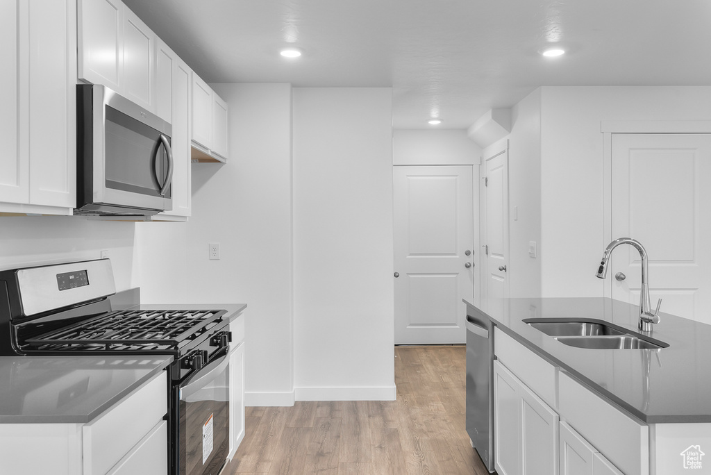 Kitchen with stainless steel appliances, dark countertops, light wood-style flooring, white cabinetry, and a sink