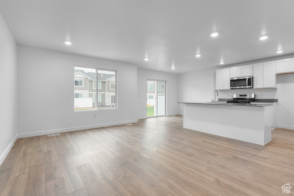 Kitchen with white cabinets, light wood-style floors, stainless steel appliances, and open floor plan
