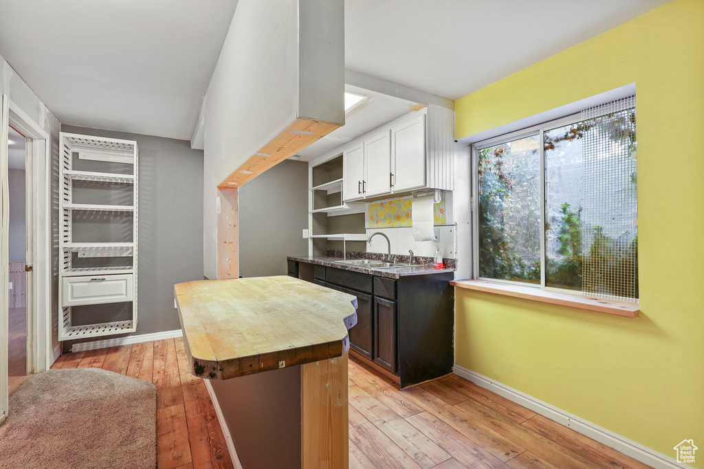 Kitchen featuring light wood finished floors, baseboards, butcher block counters, white cabinetry, and a sink