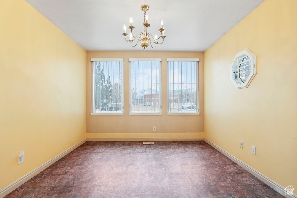 Spare room with baseboards, plenty of natural light, and an inviting chandelier