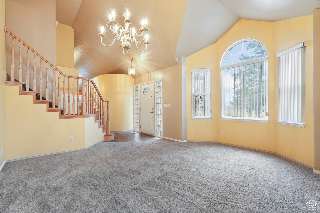 Entryway with high vaulted ceiling, stairway, carpet, and a notable chandelier