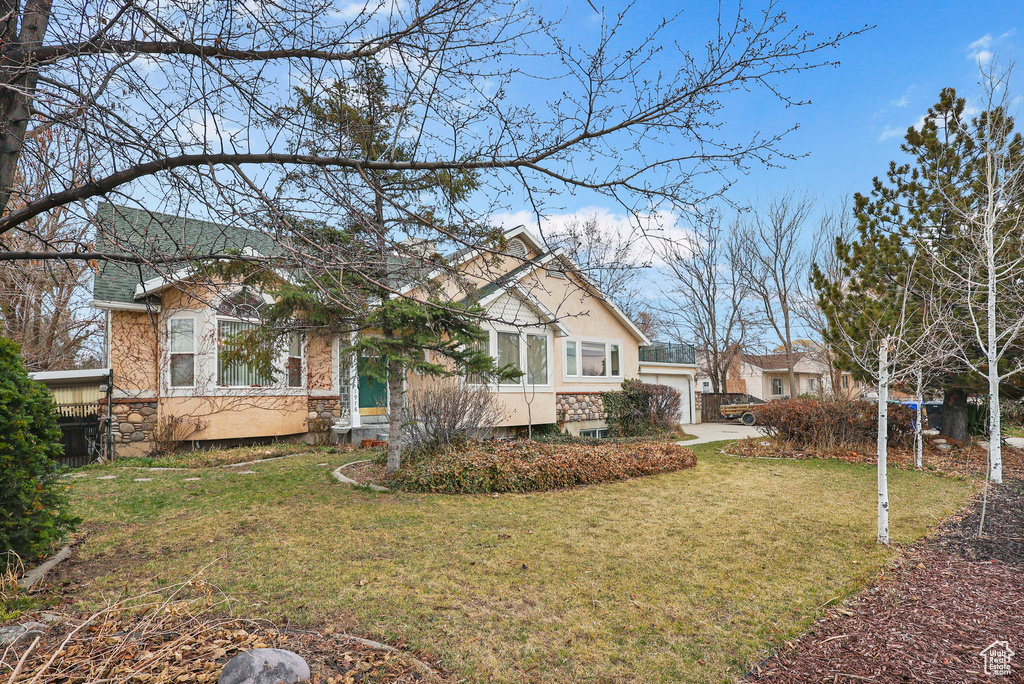 View of front of home with a garage, stone siding, a front yard, and stucco siding