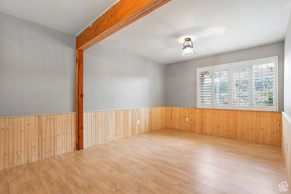 Spare room with wainscoting, wood walls, beamed ceiling, and wood finished floors