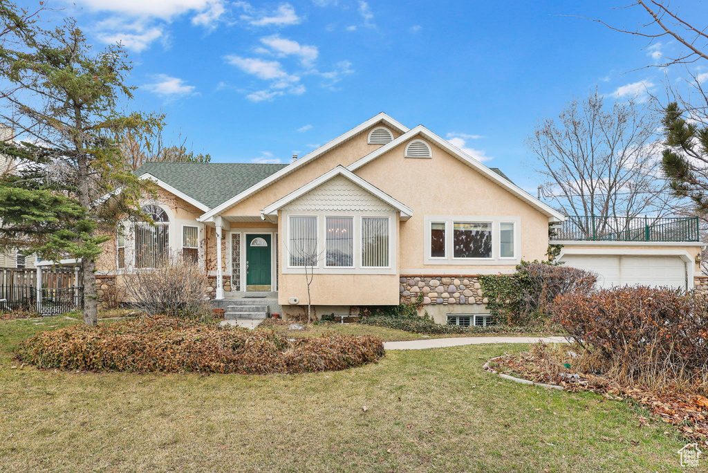 View of front of property with stucco siding, fence, a garage, stone siding, and a front lawn