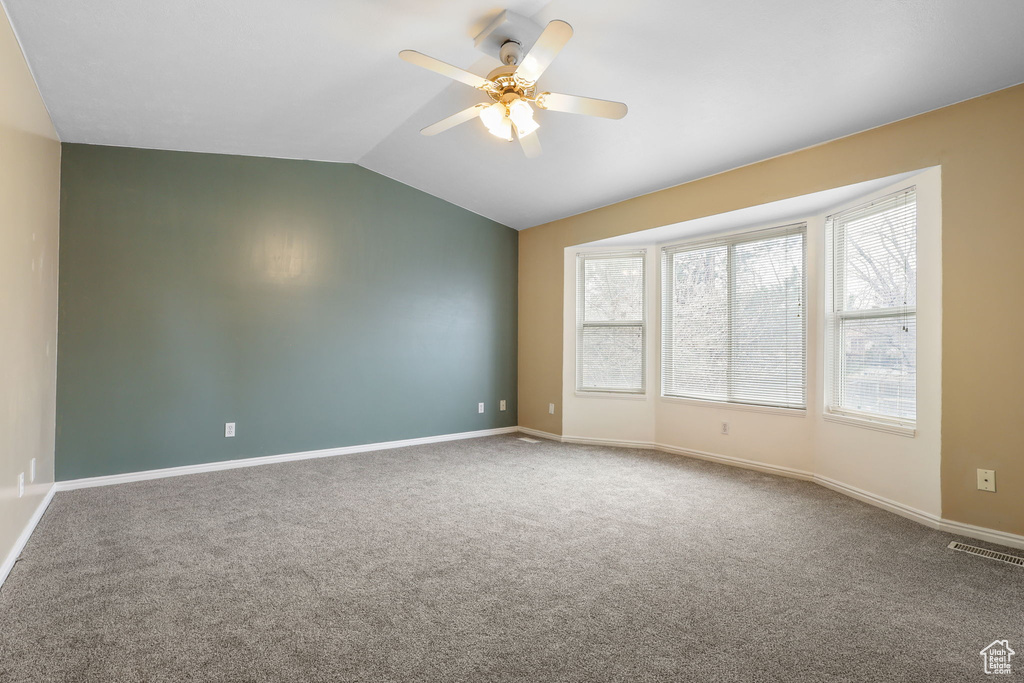 Carpeted empty room with ceiling fan, baseboards, visible vents, and vaulted ceiling