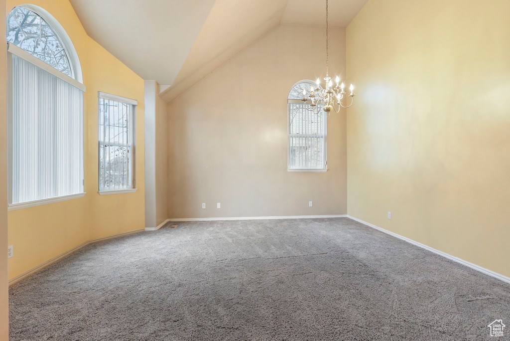 Carpeted spare room featuring a chandelier, high vaulted ceiling, a wealth of natural light, and baseboards