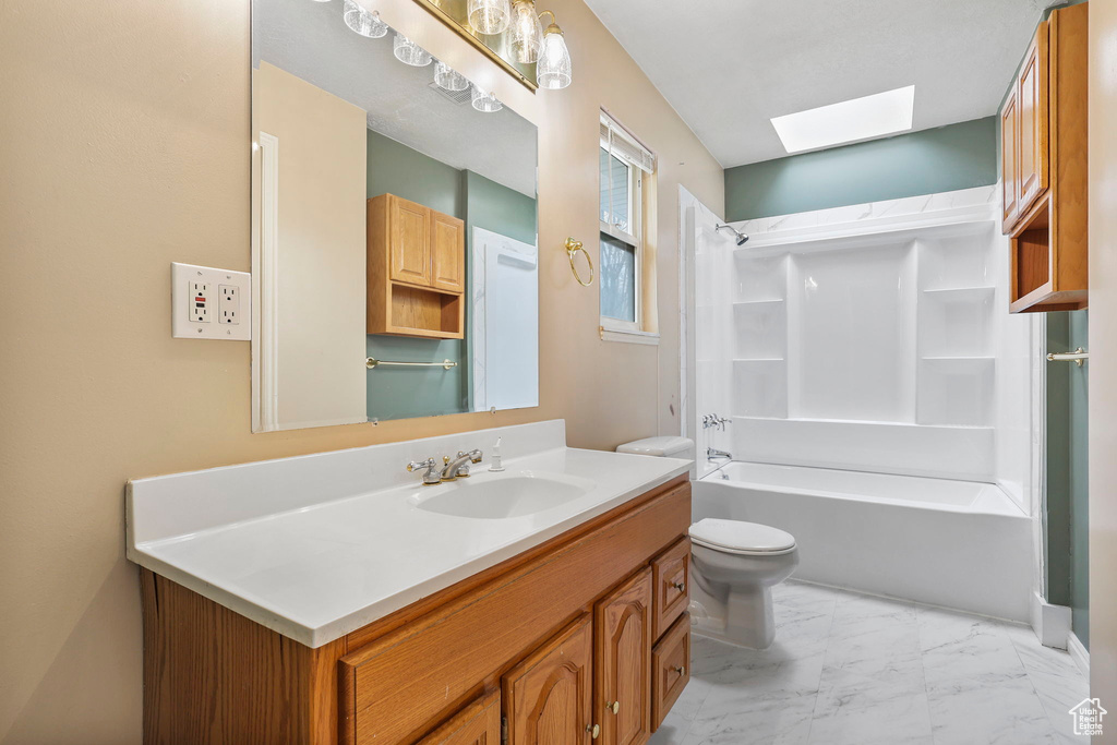 Full bathroom with toilet, a skylight, vanity, marble finish floor, and tub / shower combination