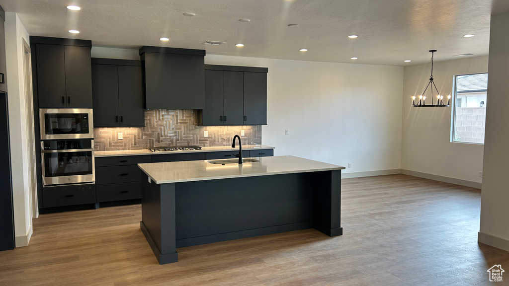 Kitchen with range hood, a sink, light countertops, an inviting chandelier, and stainless steel appliances