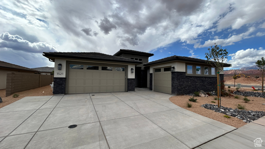 Prairie-style home featuring a garage, stucco siding, driveway, and stone siding