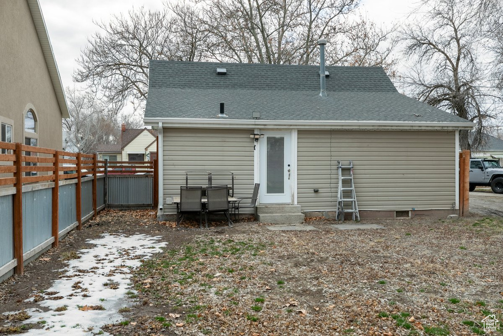 Rear view of house featuring a shingled roof, entry steps, and fence