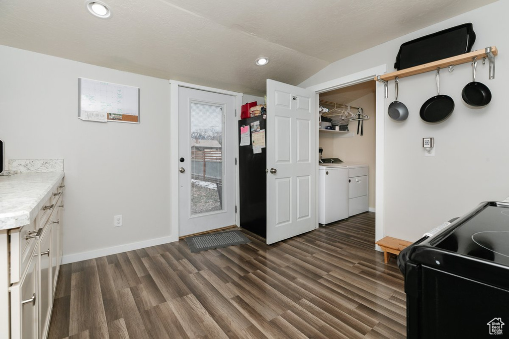 Kitchen featuring dark wood-style floors, light countertops, washing machine and dryer, vaulted ceiling, and black appliances