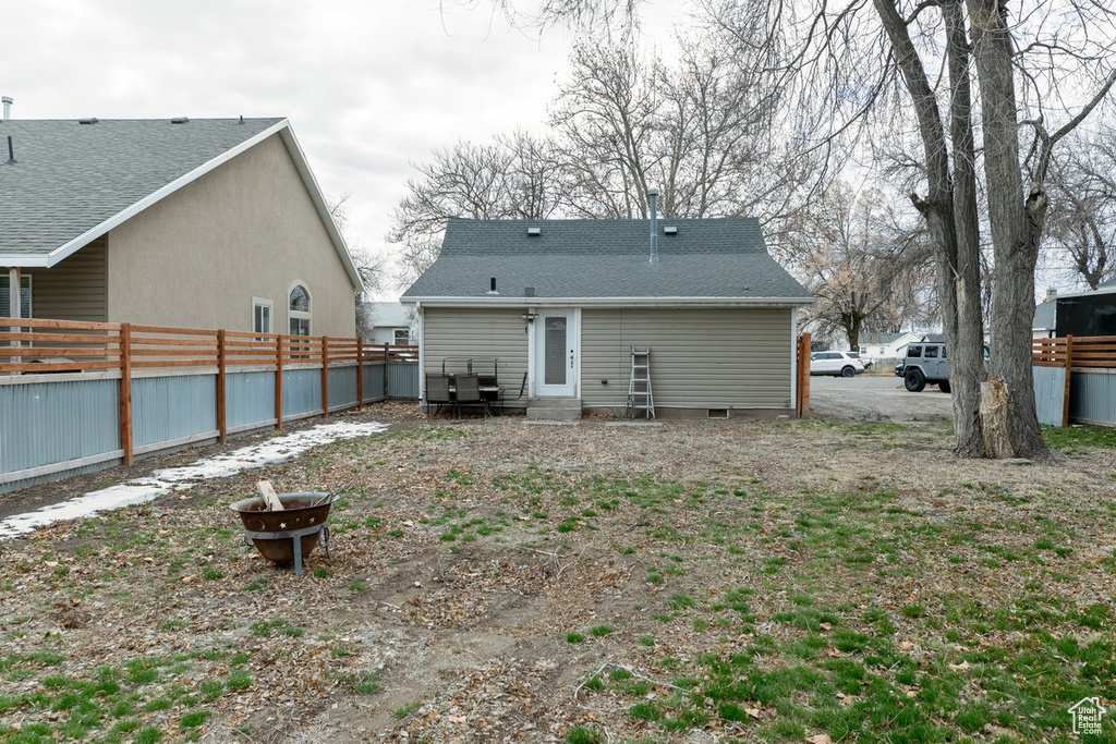 Rear view of house with an outdoor fire pit, a shingled roof, and fence