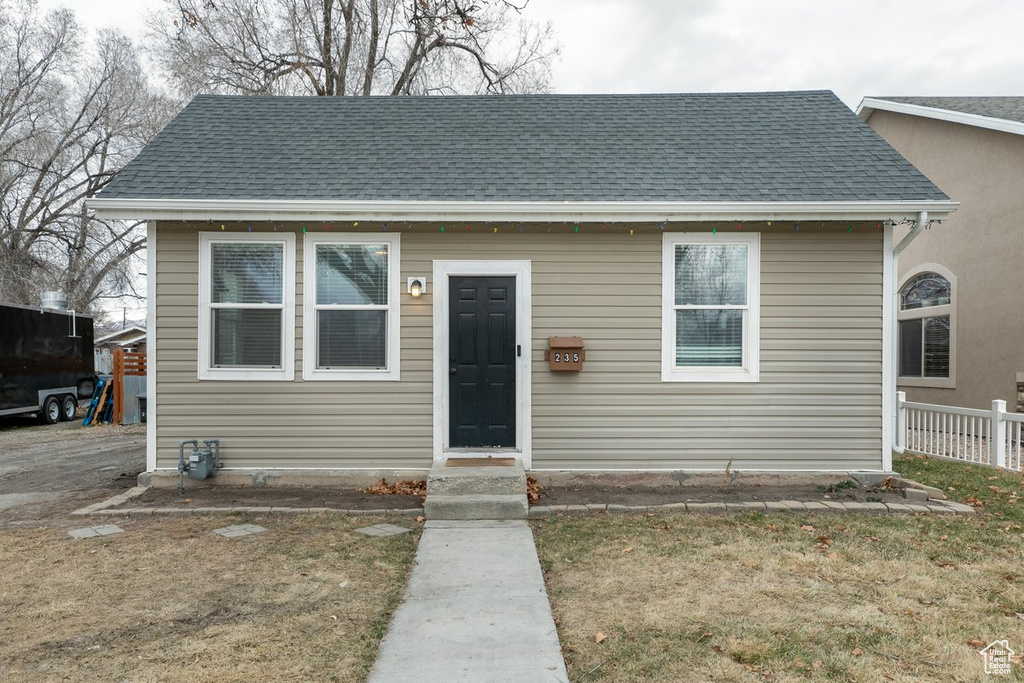 Bungalow-style home with a shingled roof and fence