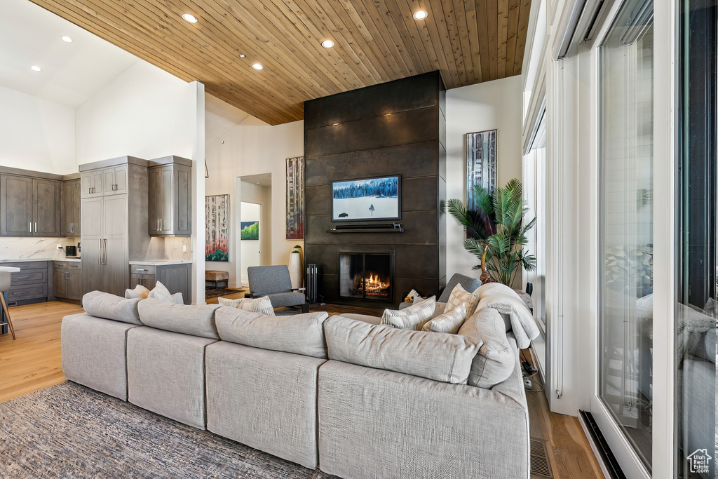Living room with wooden ceiling, light wood-style floors, high vaulted ceiling, recessed lighting, and a fireplace