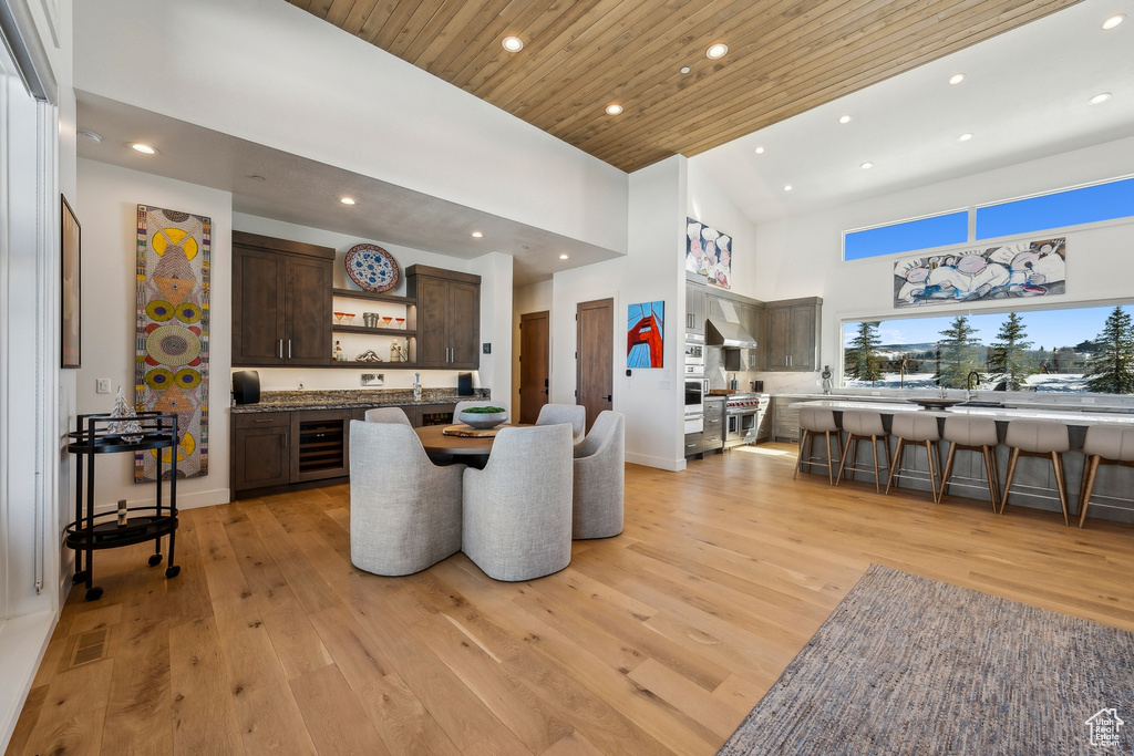 Dining space featuring beverage cooler, recessed lighting, high vaulted ceiling, wet bar, and light wood finished floors